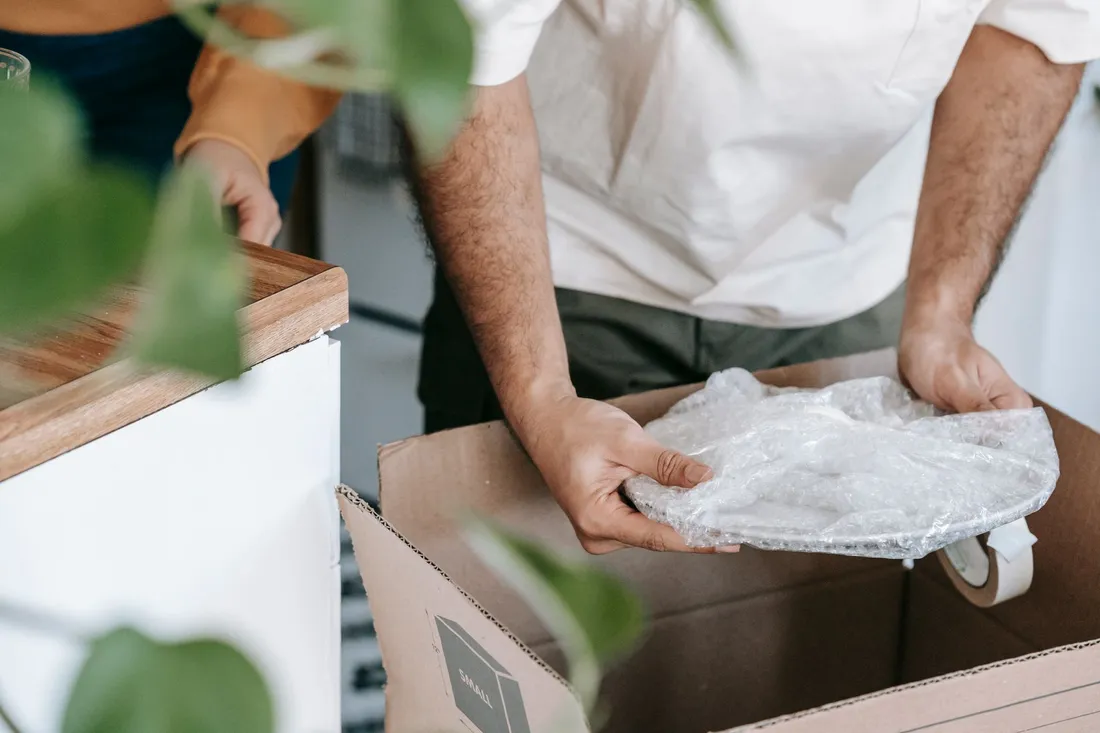 Packhelfer verpackt Geschirr aus der Küche sorgfältig in einen Umzugskarton